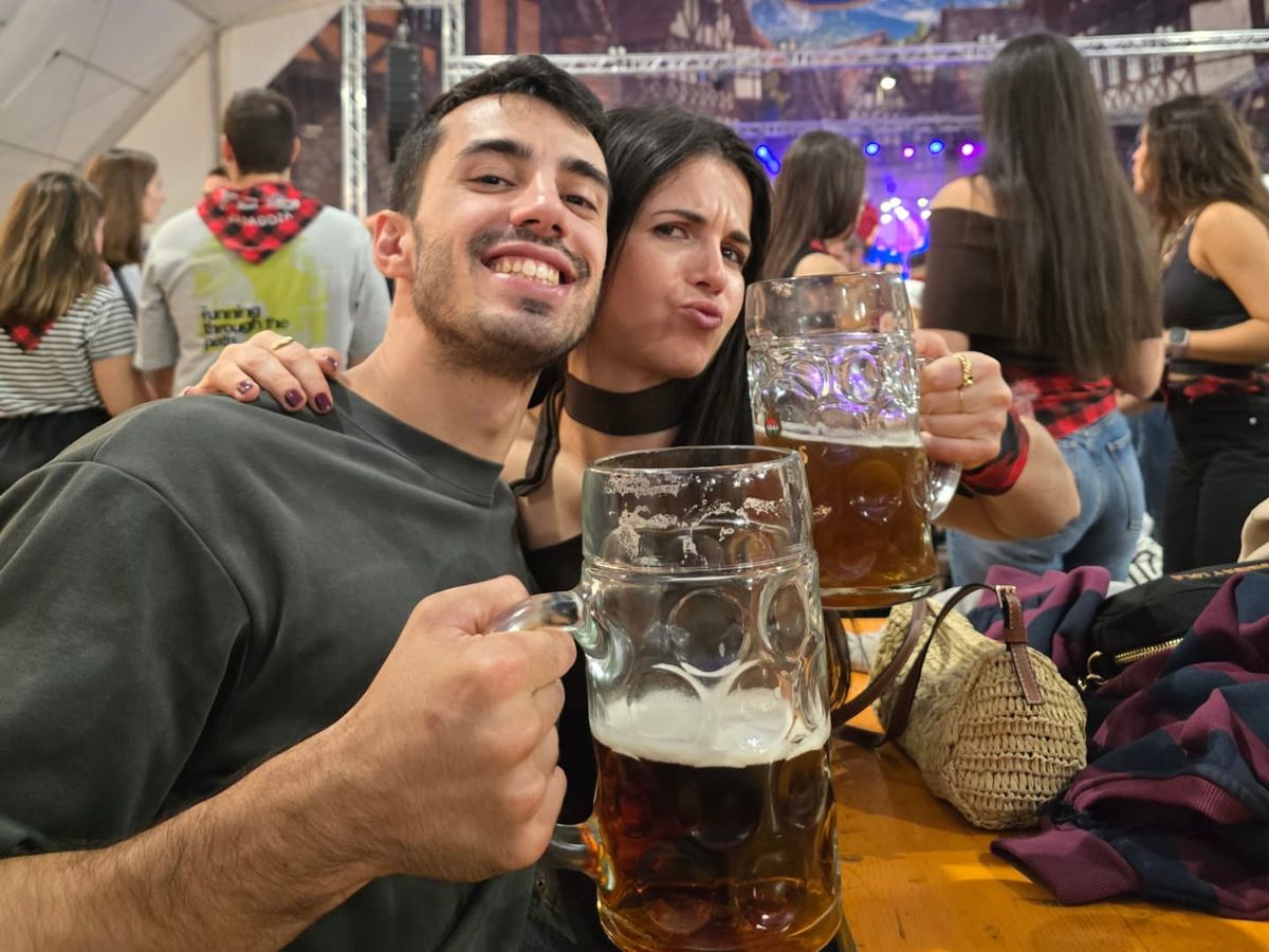 David y Lucía brindando con dos jarras de cerveza en una carpa de fiestas.
